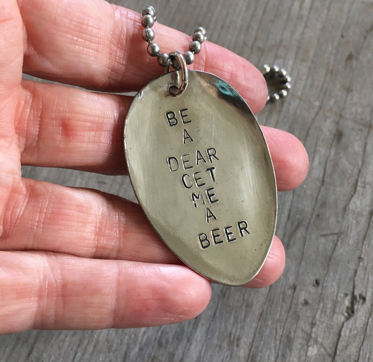 BE A DEAR GET ME A BEER stamped spoon necklace held in hand for scale showing layerable gypsy-spirited style, one-of-a-kind bold jewelry
