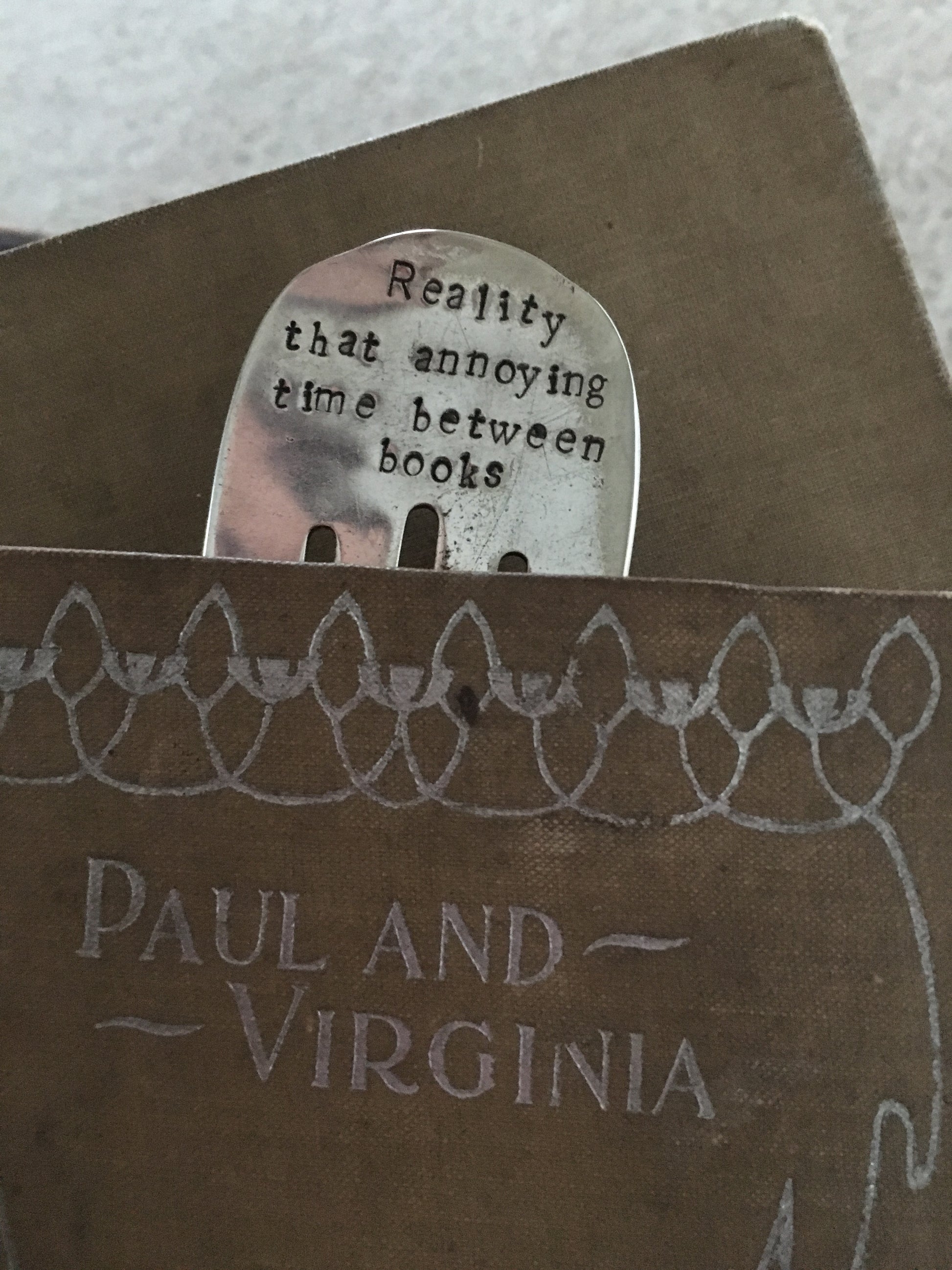 Upcycled fork bookmark with sassy hand-stamped saying REALITY THAT ANNOYING TIME BETWEEN BOOKS - shown in a book