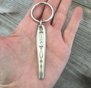 Silverware handle keychain stamped HOME shown in hand for sca;e