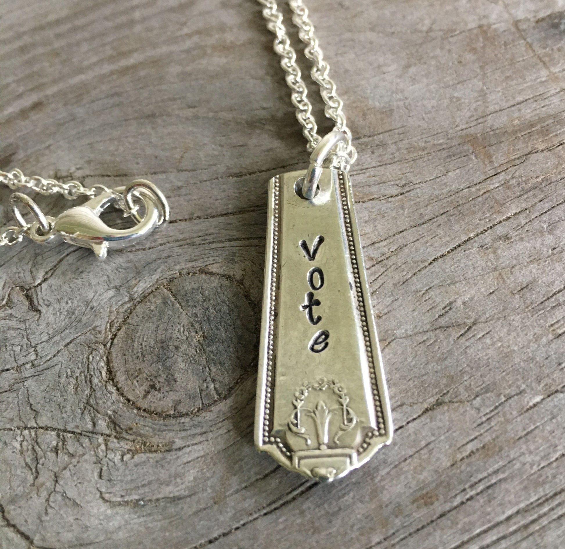 Close-up detail of VOTE bar pendant showing hand-stamped lettering on vintage 1922 Homestead pattern silverware, meaningful design
