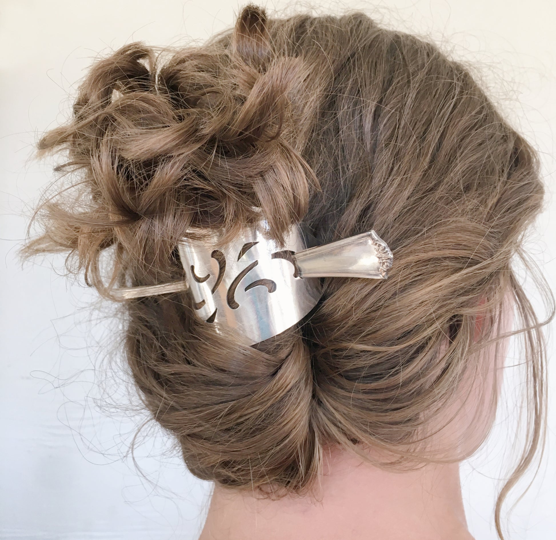 A close-up image of a half-moon shaped hair stick barrette with a vintage cake server design, featuring a silver-colored punched pattern.