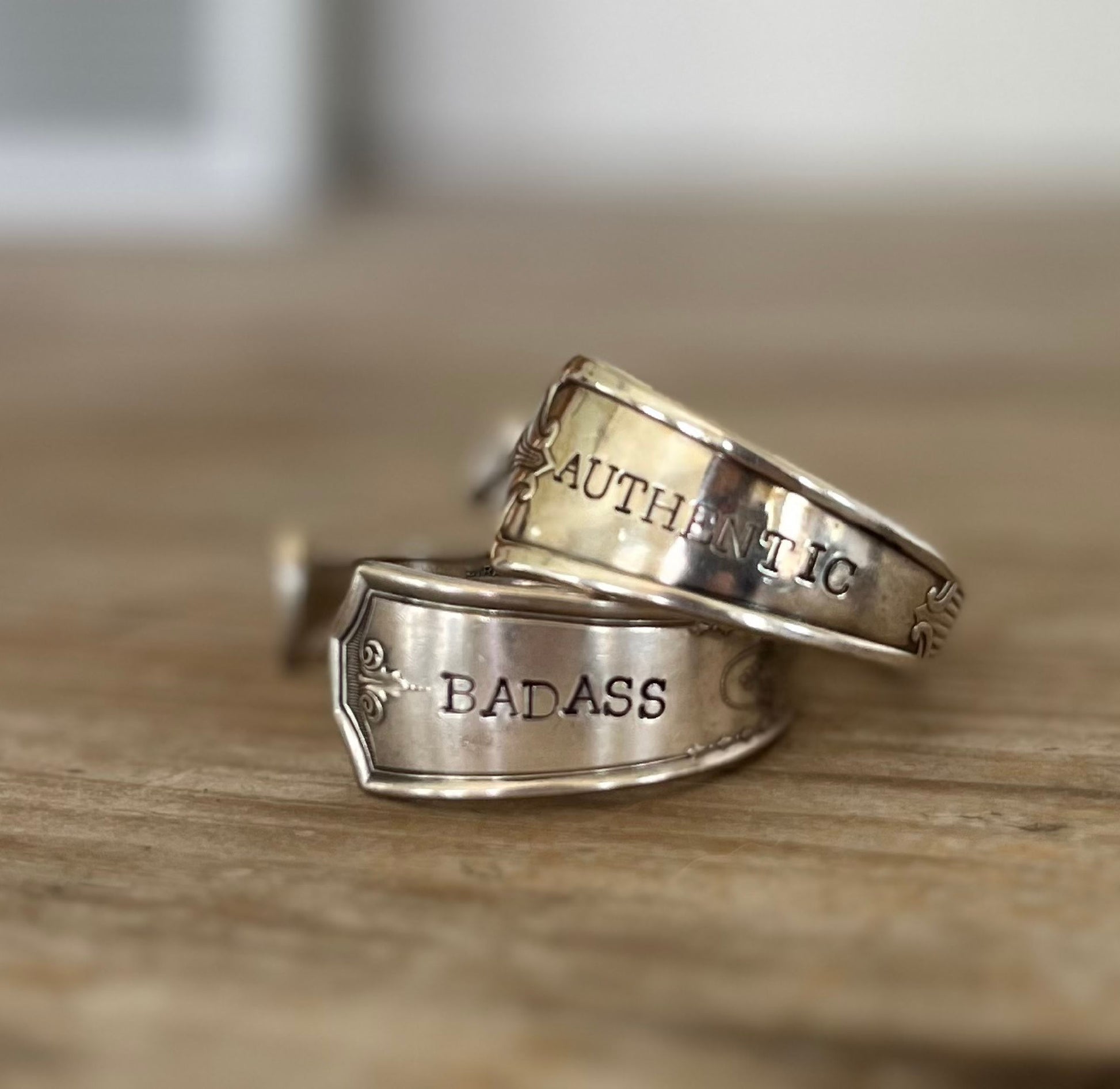 Close up of stamping on a pair of hand stamped upcycled spoon cuff bracelets stamped with BADASS and AUTHENTIC