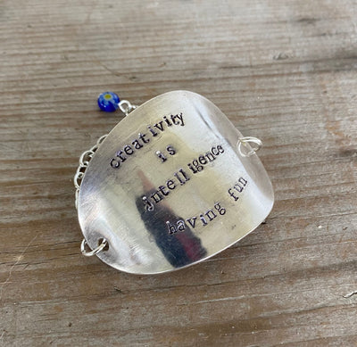 Close-up of hand-stamped Einstein quote and vibrant cobalt millefiori bead detail on flattened vintage spoon bowl bracelet