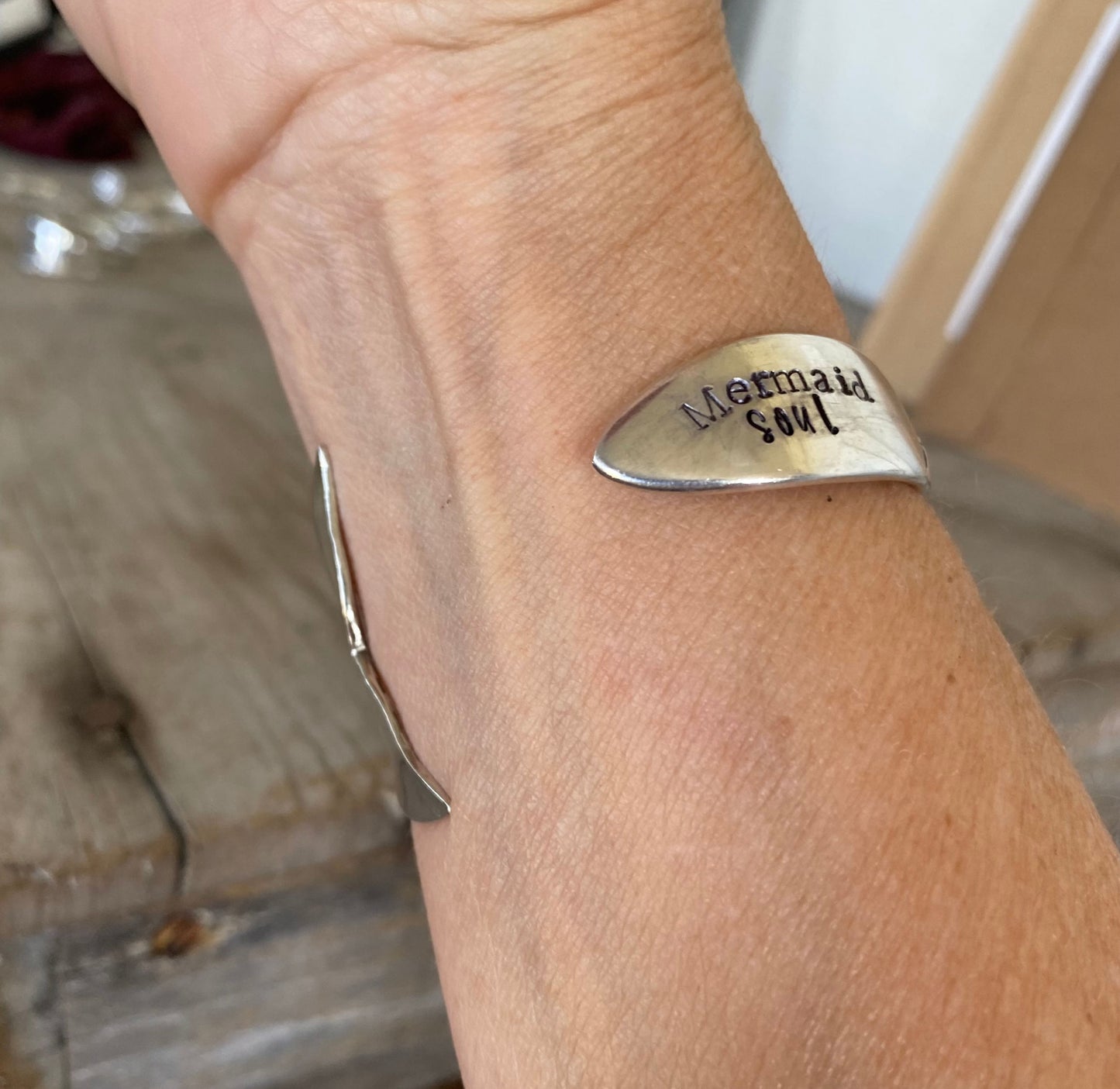 Upcycled silverware mermaid cuff bracelet worn on wrist, showing hand-carved fin, hand stamping and adjustable fit