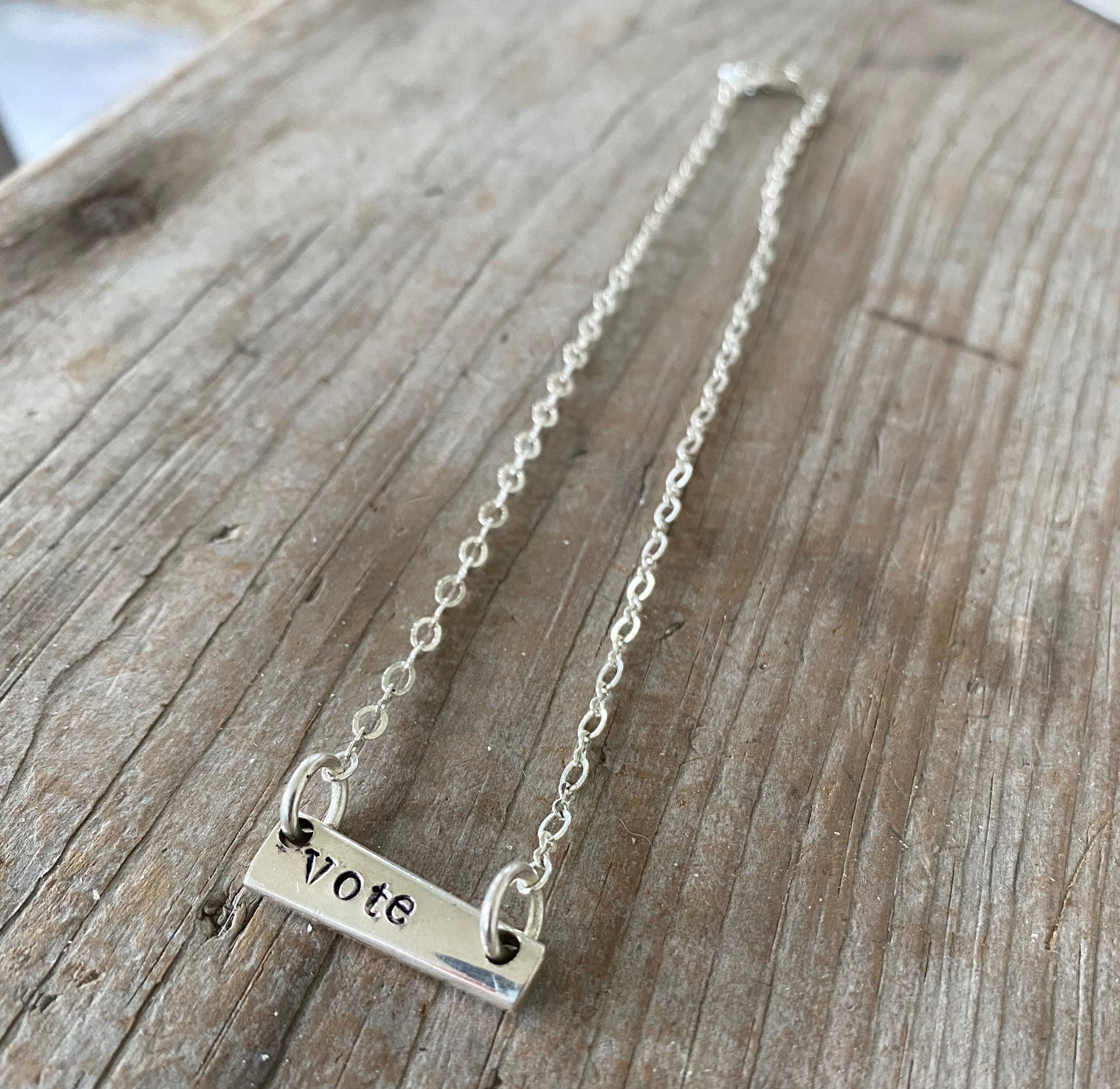 Close-up detail of VOTE bar choker showing hand-stamped lettering on vintage silverware, sits at collarbone, 6.5-inch drop
