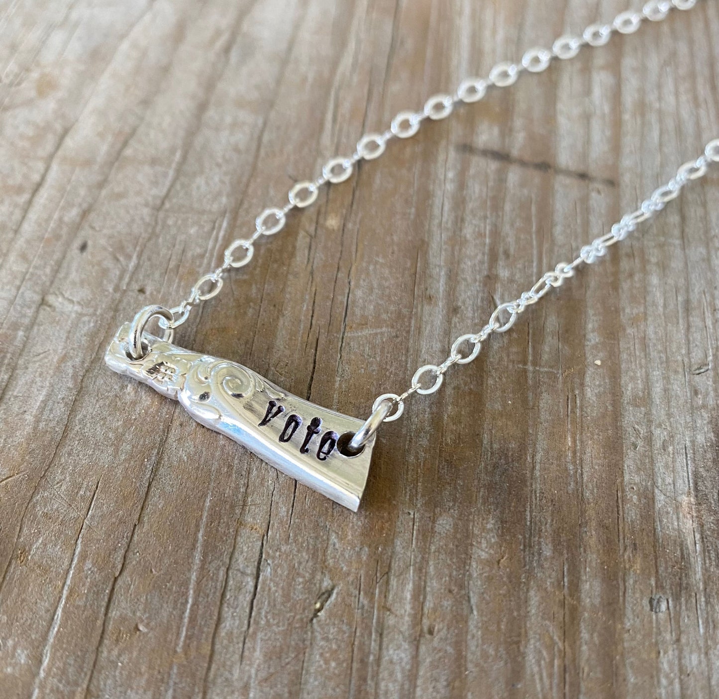 Close-up detail of VOTE bar pendant showing hand-stamped lettering on vintage silverware, 1.25 inches wide