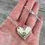 Close-up of Hiawatha spoon heart pendant showing vintage rhinestone earring flower detail, upcycled 1939 William Rogers silverware necklace - shown in hand for scale