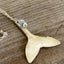 Close-up of vintage silverplate spoon whale tail pendant showing contoured shape and light blue ocean bead accent detail