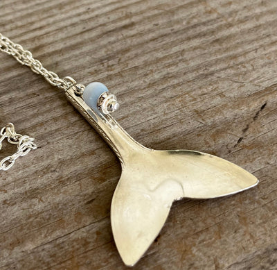 Close-up of vintage silverplate spoon whale tail pendant showing contoured shape and light blue ocean bead accent detail