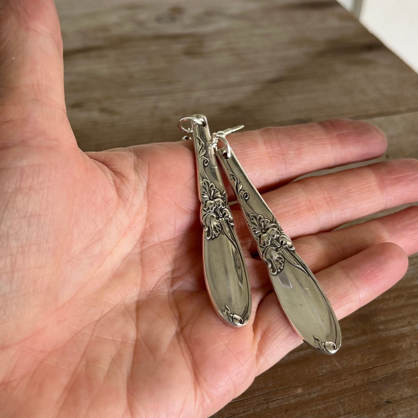 White Orchid spoon earrings held in hand for scale showing teardrop shape and Community Silverplate detail