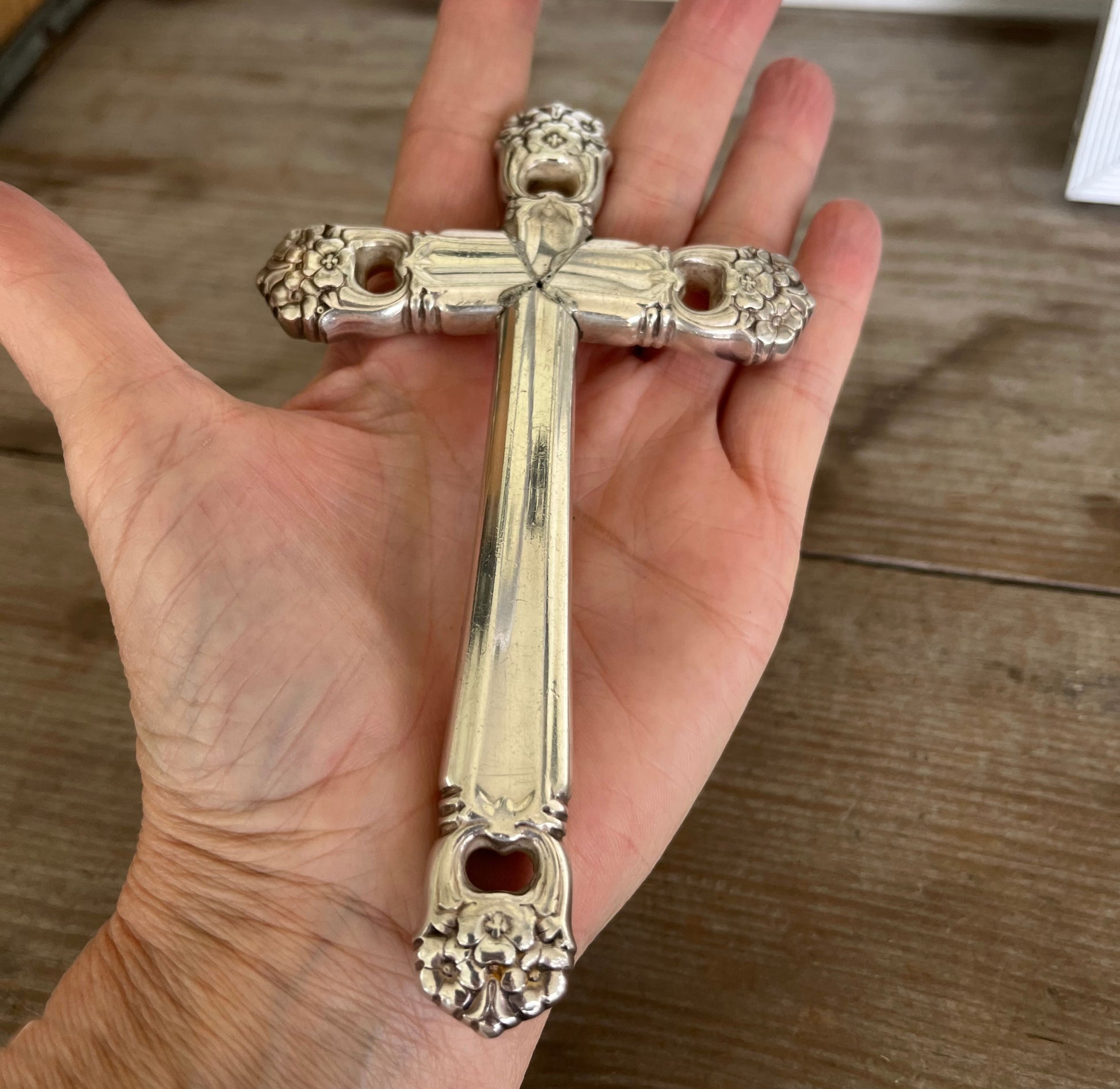 Artisan upcycled knife cross - four hollow handles forming devotional page weight - shown in hand for scale