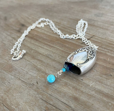 Close-up detail of handcrafted knife bell pendant showing Lady Densmore silverplate pattern and blue bead clapper