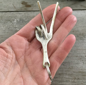 Key chain upcycled from a fork into the shape of a hand give the peace sign hand gesture shown in human hand to show size and scale