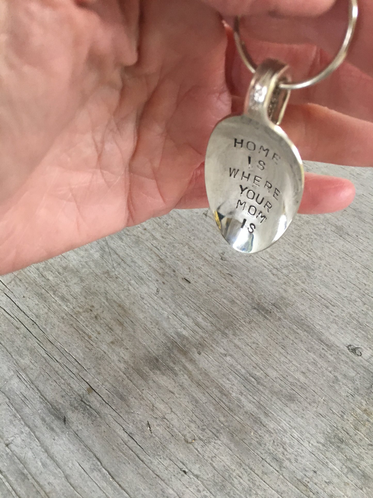 Spoon keychain hand stamped with HOME IS WHERE your mom is shown in hand for size and scale