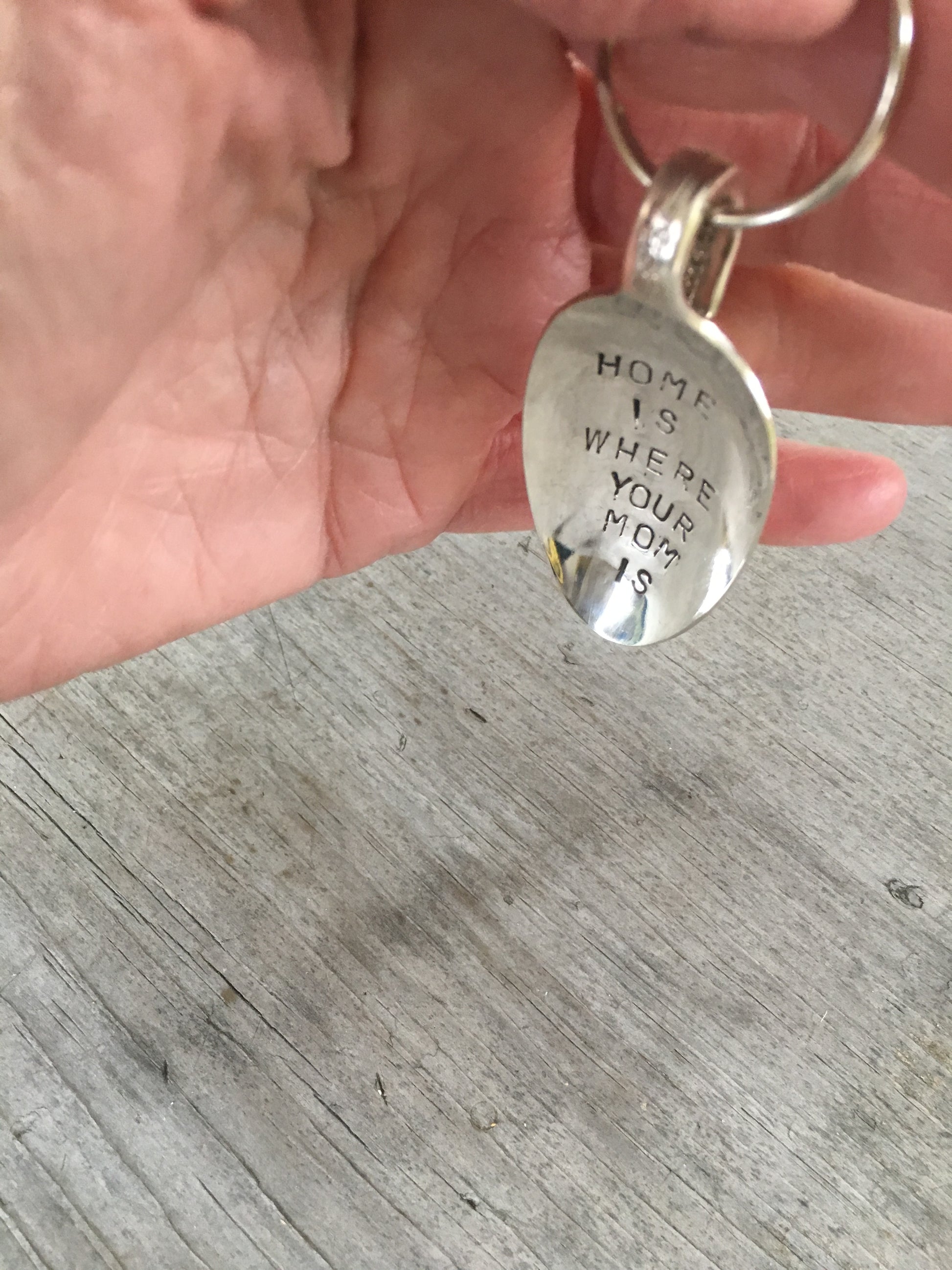 Spoon keychain hand stamped with HOME IS WHERE your mom is shown in hand for size and scale