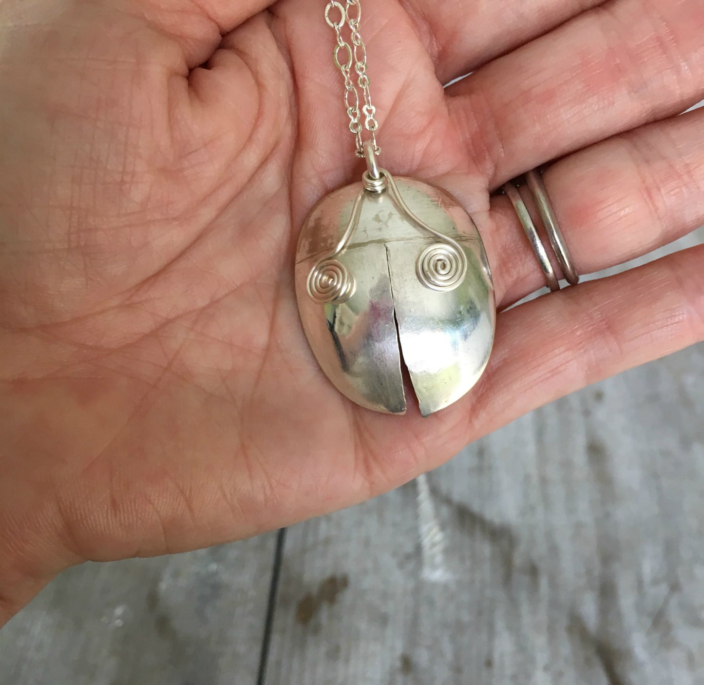 Upcycled Spoon Handmade into a Ladybug Necklace Shown in hand for scale