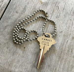 Key Necklace stamped with Wander and an airstream camper hanging form a vintage ball chain