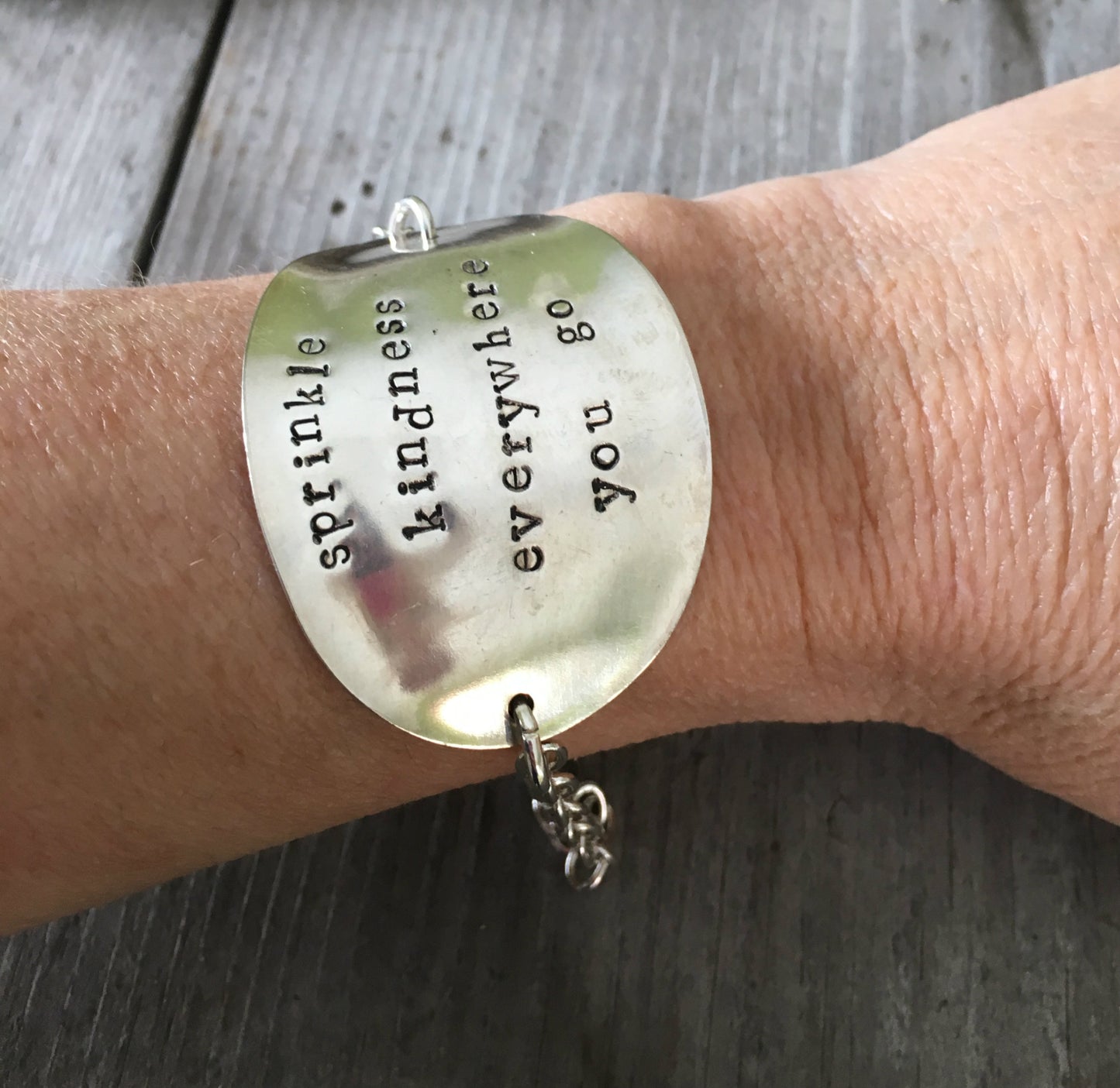 Upcycled spoon bracelet hand stamped with sprinkle kindness everywhere you go shown on models arm