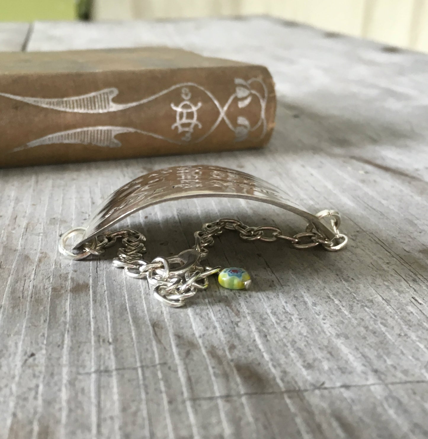 Side view of hand-stamped vintage spoon bracelet with 'Teaching Is My Super Power' message and bright yellow millefiori glass bead