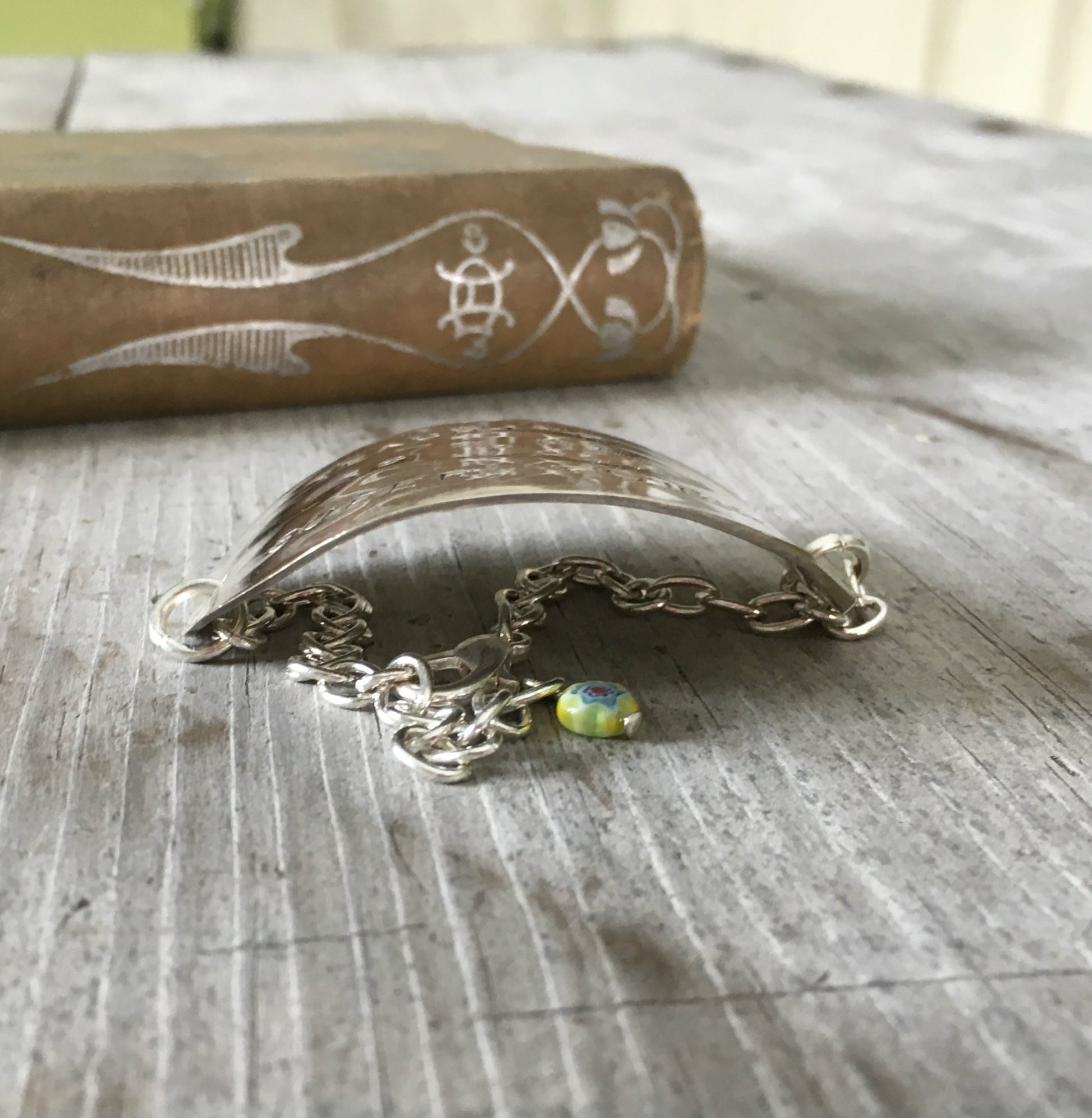 Side view of hand-stamped vintage spoon bracelet with 'Teaching Is My Super Power' message and bright yellow millefiori glass bead
