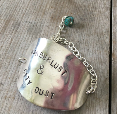 Close-up of hand-stamped wanderlust lettering and earthy turquoise glass bead on flattened vintage spoon bowl bracelet