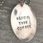 Close-up of BLOOD TYPE COFFEE hand-stamped spoon pendant showing bold lettering on reclaimed vintage silverware, caffeine-themed design