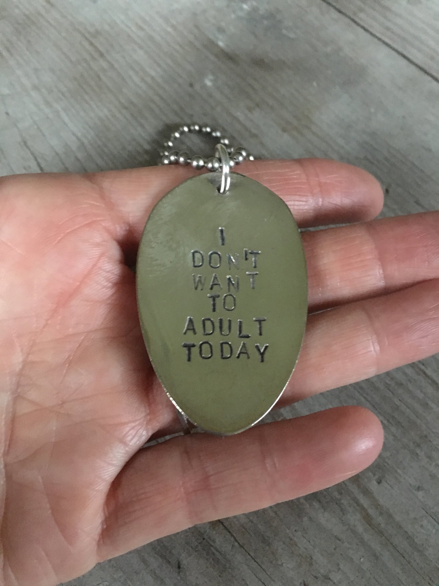 I DON'T WANT TO ADULT TODAY hand-stamped spoon necklace held in hand for scale showing vintage silverplate patina