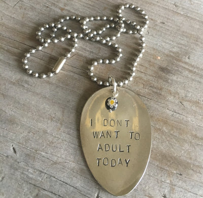 Close-up of I DON'T WANT TO ADULT TODAY hand-stamped spoon pendant showing playful message on reclaimed vintage silverware with millefiori glass bead