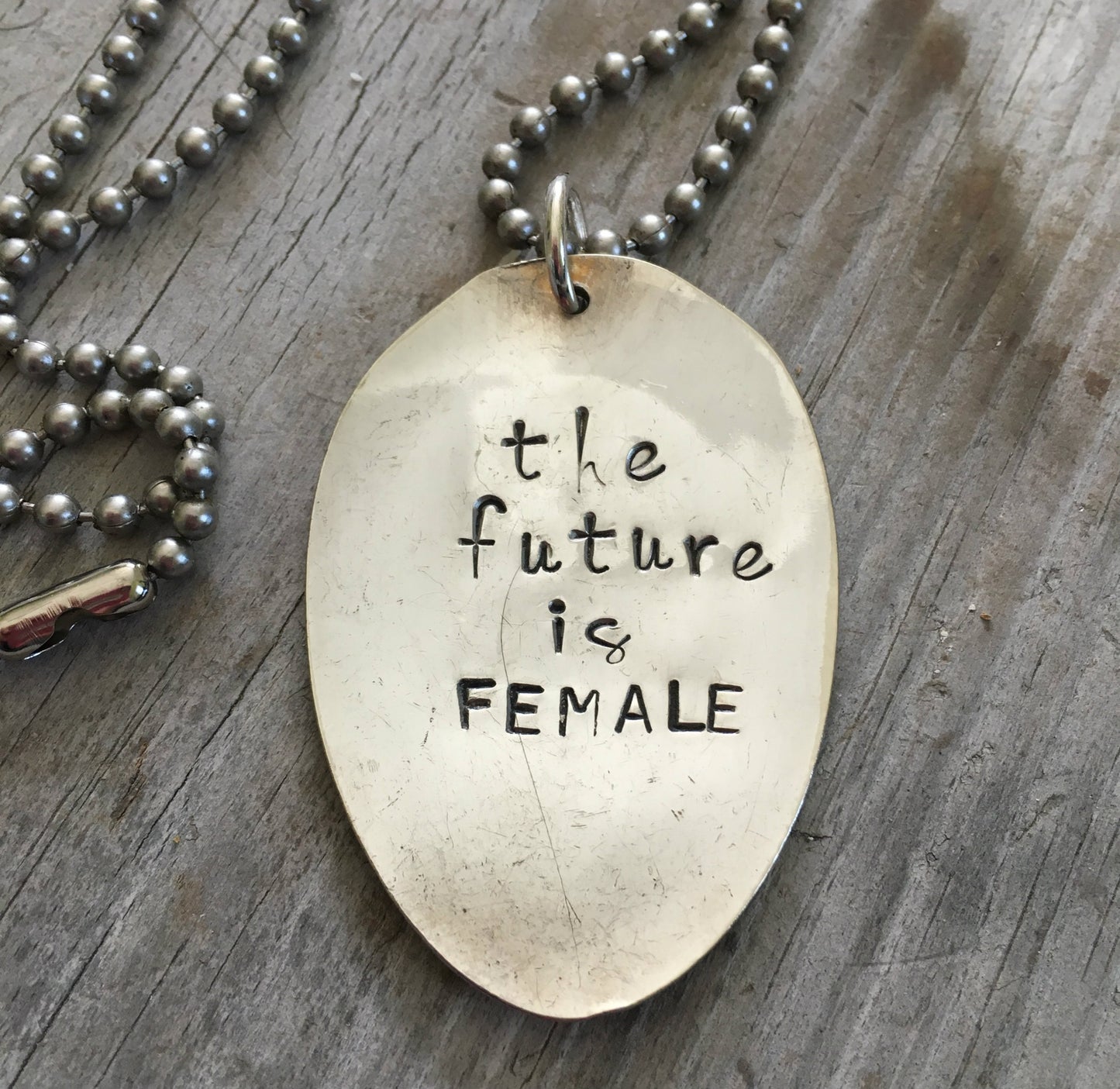 Close-up of THE FUTURE IS FEMALE hand-stamped spoon pendant showing bold message on reclaimed vintage silverware, empowering design