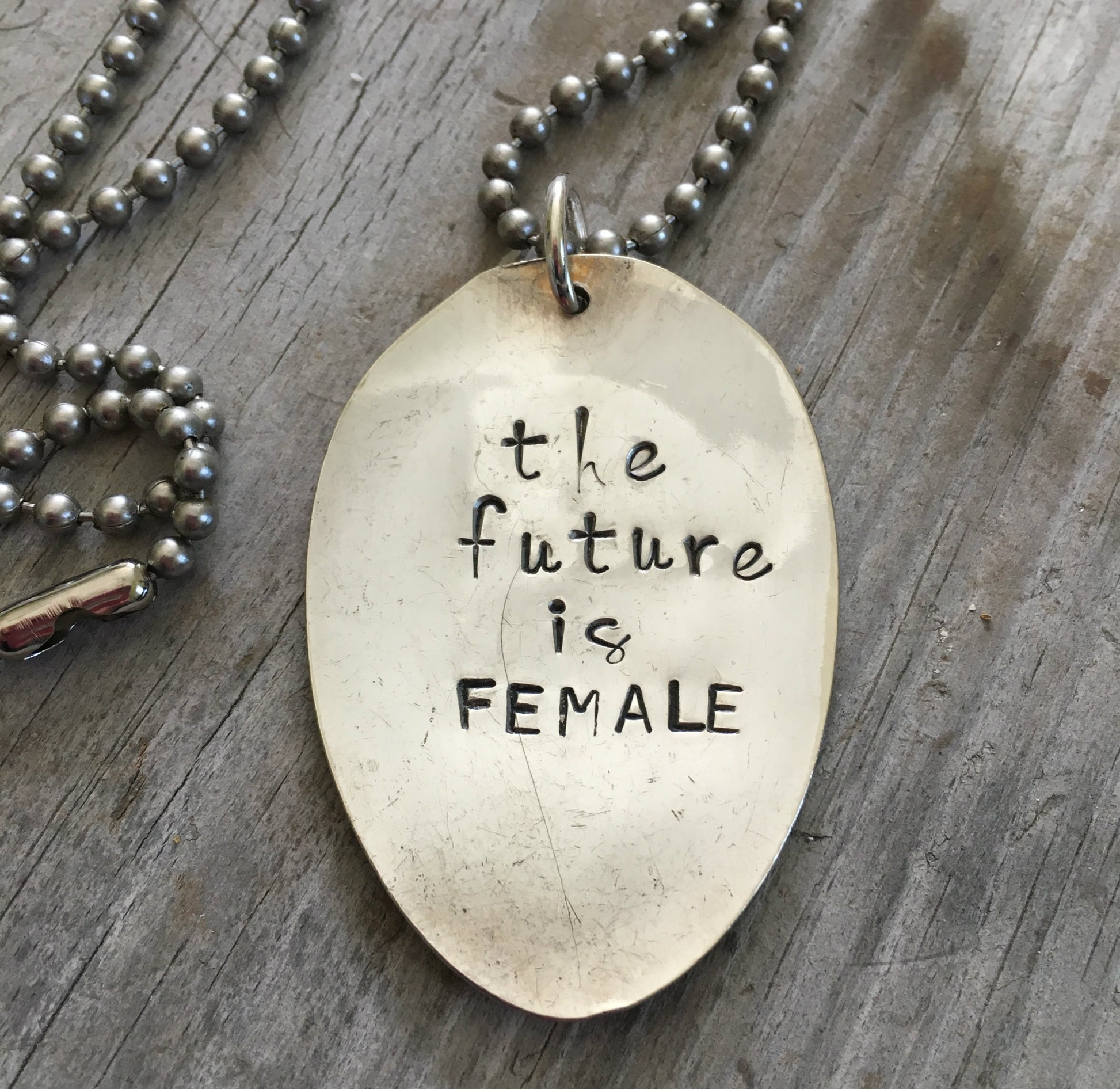 Close-up of THE FUTURE IS FEMALE hand-stamped spoon pendant showing bold message on reclaimed vintage silverware, empowering design