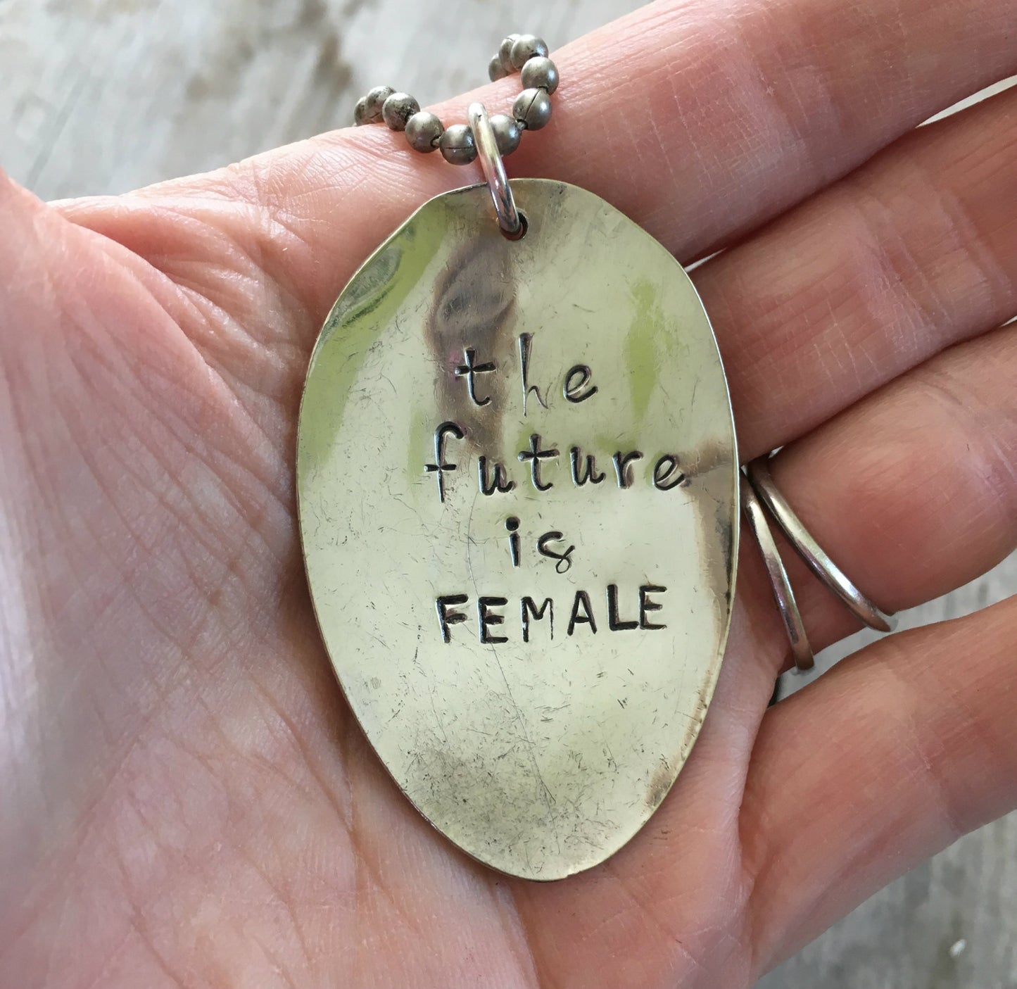 THE FUTURE IS FEMALE stamped spoon necklace held in hand for scale showing one of a kind feminist statement jewelry