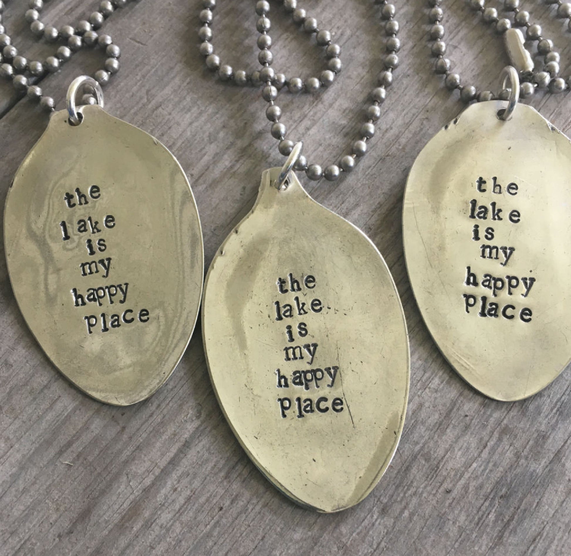 Close-up of THE LAKE IS MY HAPPY PLACE hand-stamped spoon pendant showing reclaimed vintage silverware, soulful lake-themed design