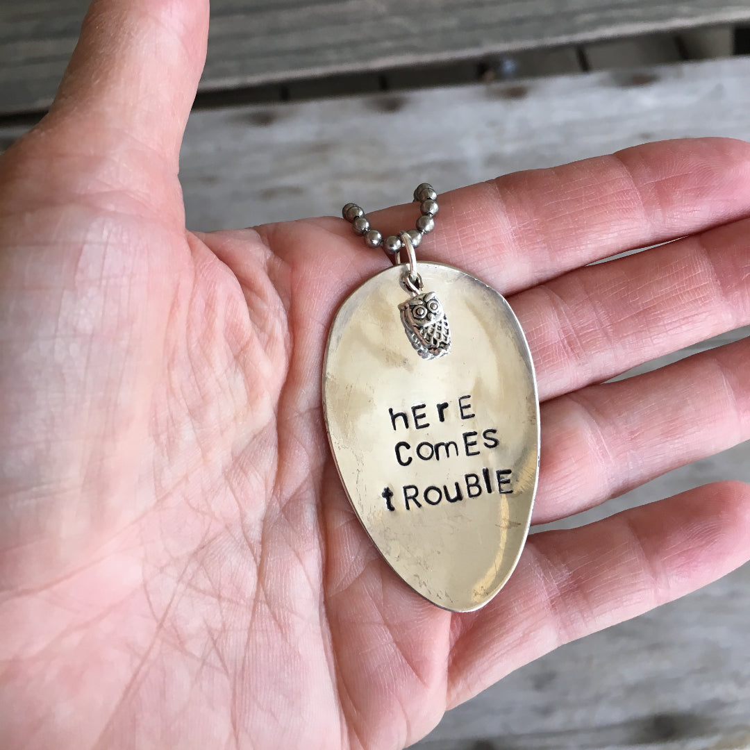Stamped Spoon Necklace with Owl Charm Reads Here Comes Trouble Shown in Hand for Scale