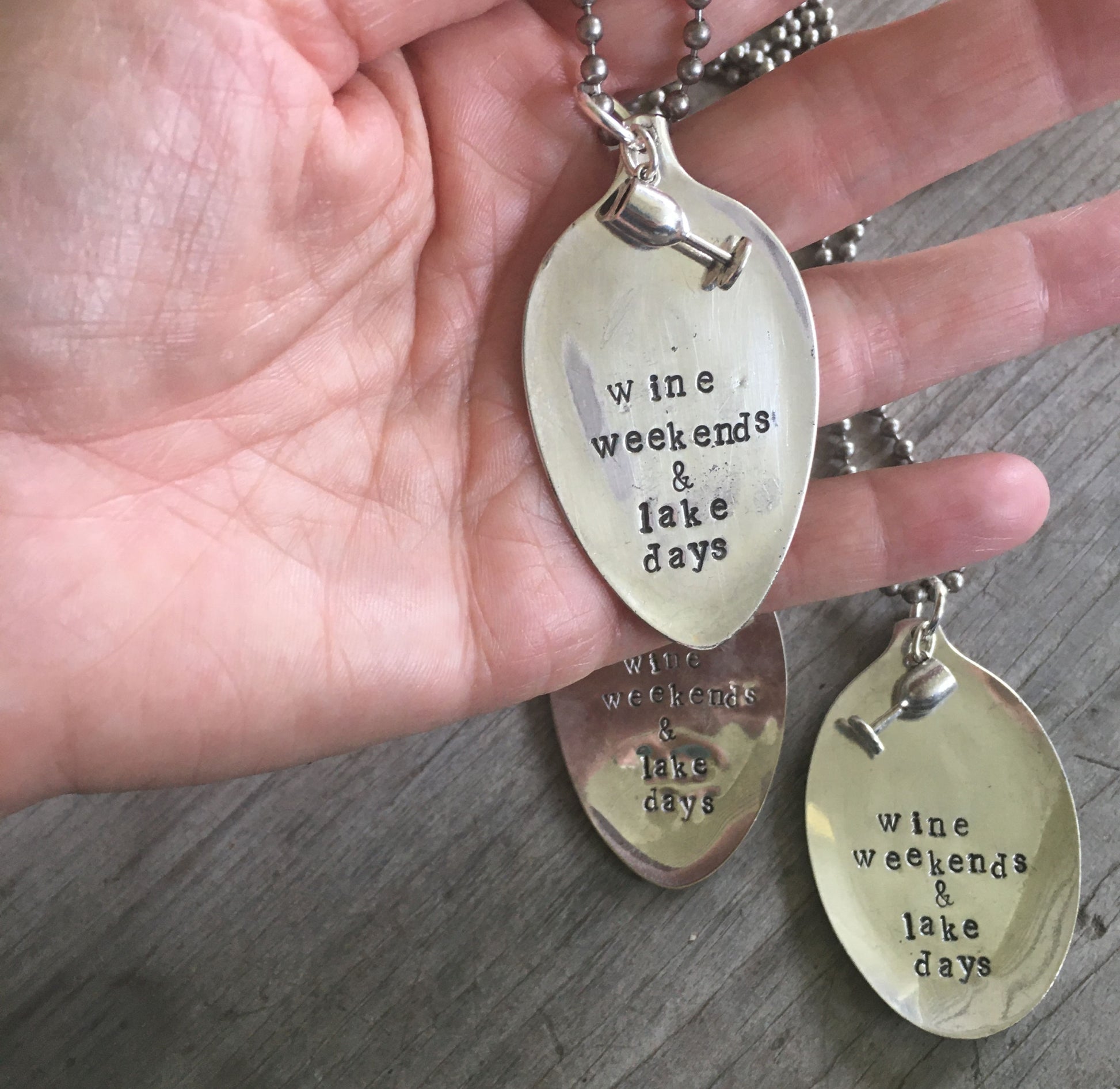 Close-up of WINE WEEKENDS & LAKE DAYS hand-stamped spoon pendant with wine glass charm showing reclaimed vintage silverware, summer-inspired design